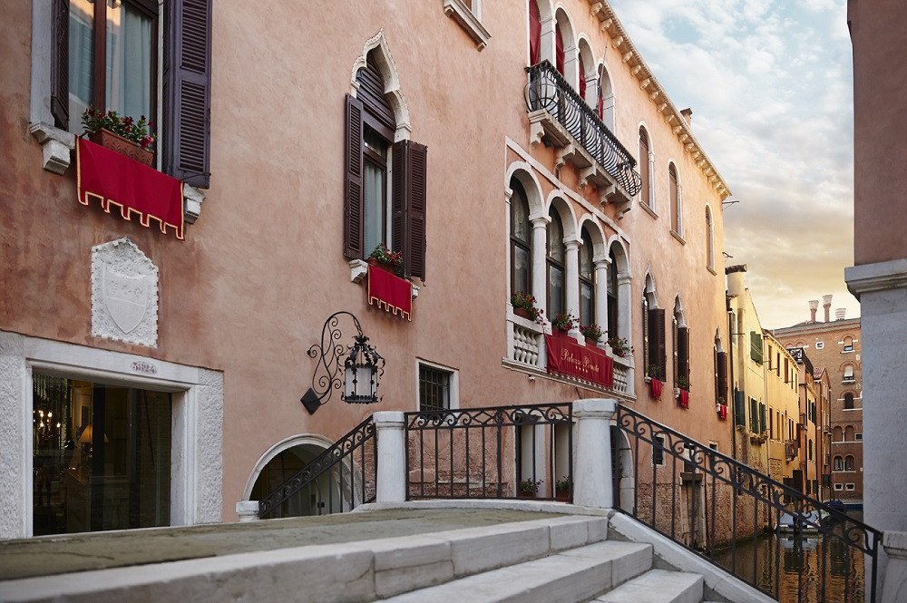 La fachada en tonos naranjas del Palazzo Paruta Hotel sobre uno de los canales de Venecia con banderas rojas. 